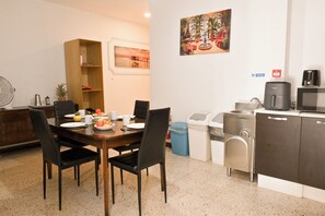 A dining area with a table set for four, chairs, a coffee maker, a microwave, and a trash bin. - Sea Breeze Bay Guesthouse - B3, Saint Paul's Bay, Malta (Saint Paul's Bay)