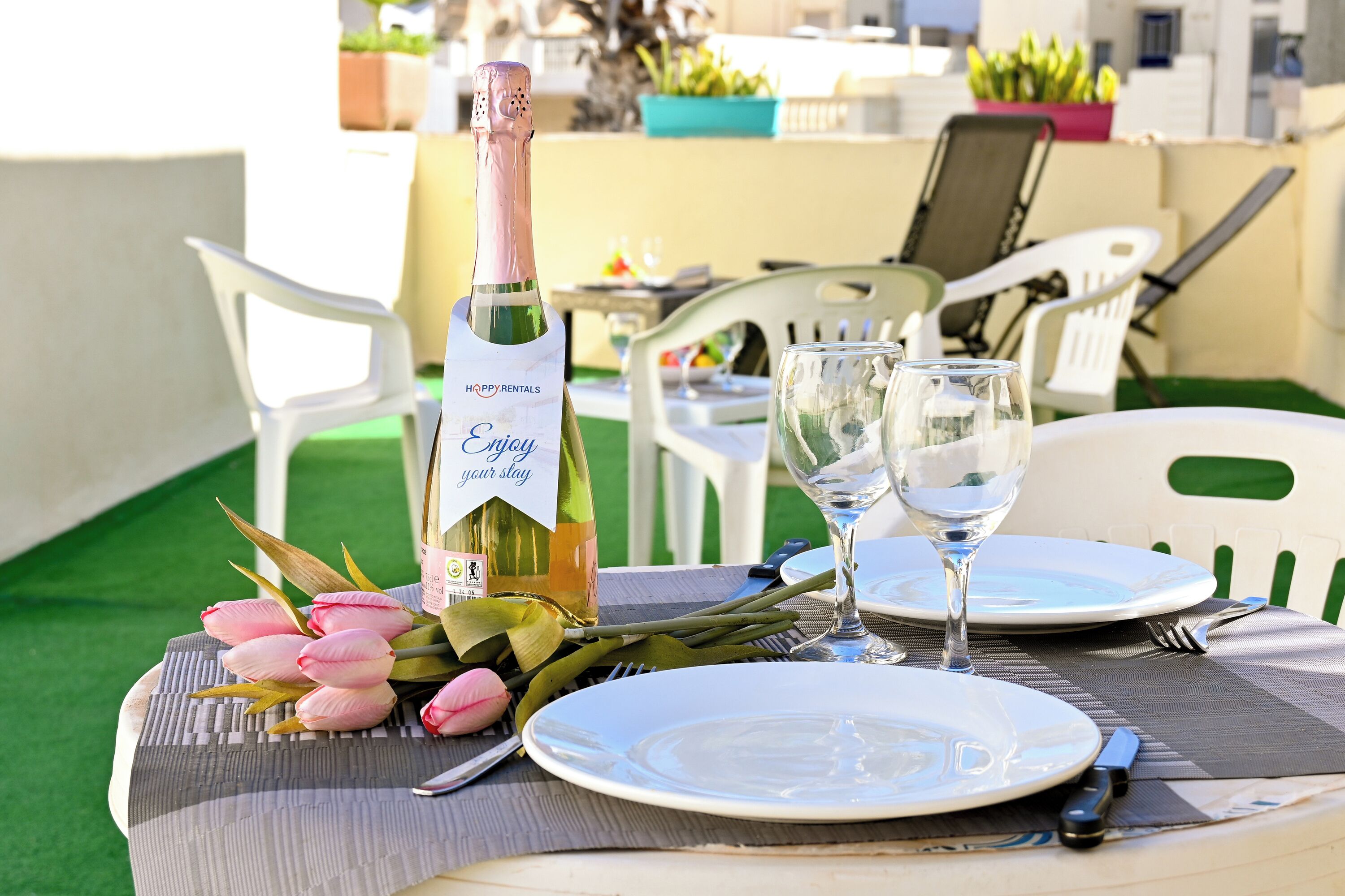 Una mesa dispuesta con una botella de vino, copas, platos y un ramo de flores.