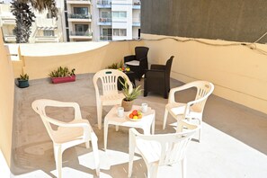 A balcony with white plastic chairs, a small table with fruit, and potted plants. - Sea Breeze Bay Guesthouse - B2, Saint Paul's Bay, Malta (Saint Paul's Bay)