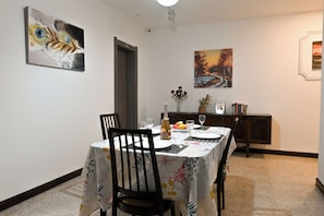 Un coin repas avec une table dressée pour deux personnes, des chaises, un meuble contenant des livres et des œuvres d’art accrochées aux murs.
