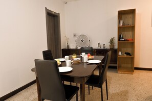 A dining area with a table set for two, chairs, a fan, and a bookshelf with various items. - Sea Breeze Bay Guesthouse - B1, Saint Paul's Bay, Malta (Saint Paul's Bay)