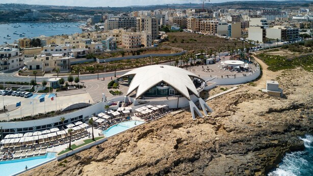 A coastal hotel with a unique white dome structure, a pool, and a view of the sea and cityscape. - Sunny Ensuite by the Sea - B1, Saint Paul's Bay, Malta (Saint Paul's Bay)