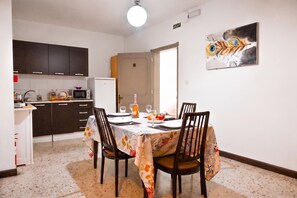 A dining area with a table set for four, kitchen cabinets, a refrigerator, and a door leading to another room. - Sunny Ensuite by the Sea - B1, Saint Paul's Bay, Malta (Saint Paul's Bay)