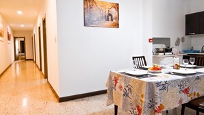Un comedor con una mesa preparada para dos, un cuadro en la pared y una cocina al fondo.