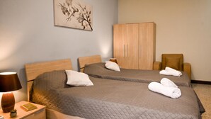 Et hotelværelse med to senge, en træskab, et skrivebord med lampe og et billede på væggen.