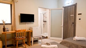 A hotel room with a bed, a desk with a chair, a TV, a shower, and a door. - Sunny Ensuite by the Sea - A3, Saint Paul's Bay, Malta (Saint Paul's Bay)