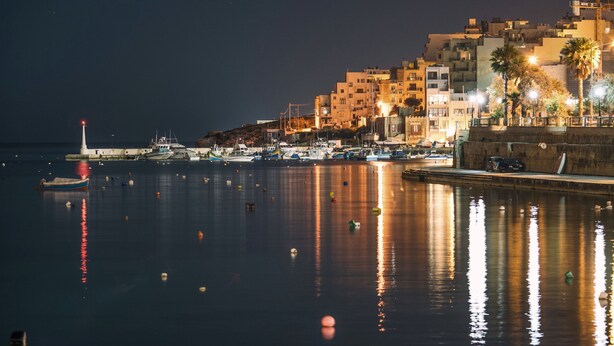 A nighttime harbor with boats, a lighthouse, and buildings along the waterfront. - Sunny Ensuite by the Sea - A3, Saint Paul's Bay, Malta (Saint Paul's Bay)