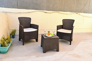 Two wicker chairs with cushions, a small table with a fruit bowl and glasses, and potted plants on a concrete floor. - Sea Breeze Bay Guesthouse - A3, Saint Paul's Bay, Malta (Saint Paul's Bay)