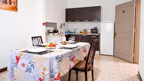 A dining area with a table set for two, a kitchen in the background, and a door to the right.