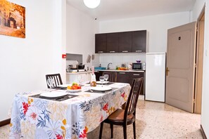 A dining area with a table set for two, a kitchen in the background, and a door to the right.