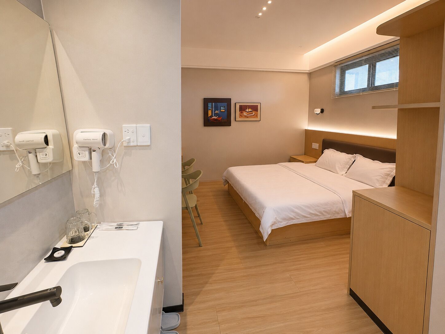 Ein modernes Hotelzimmer mit Bett, Nachttisch und Bad mit Waschbecken und Spiegel.