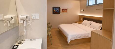 Ein modernes Hotelzimmer mit Bett, Nachttisch und Bad mit Waschbecken und Spiegel.