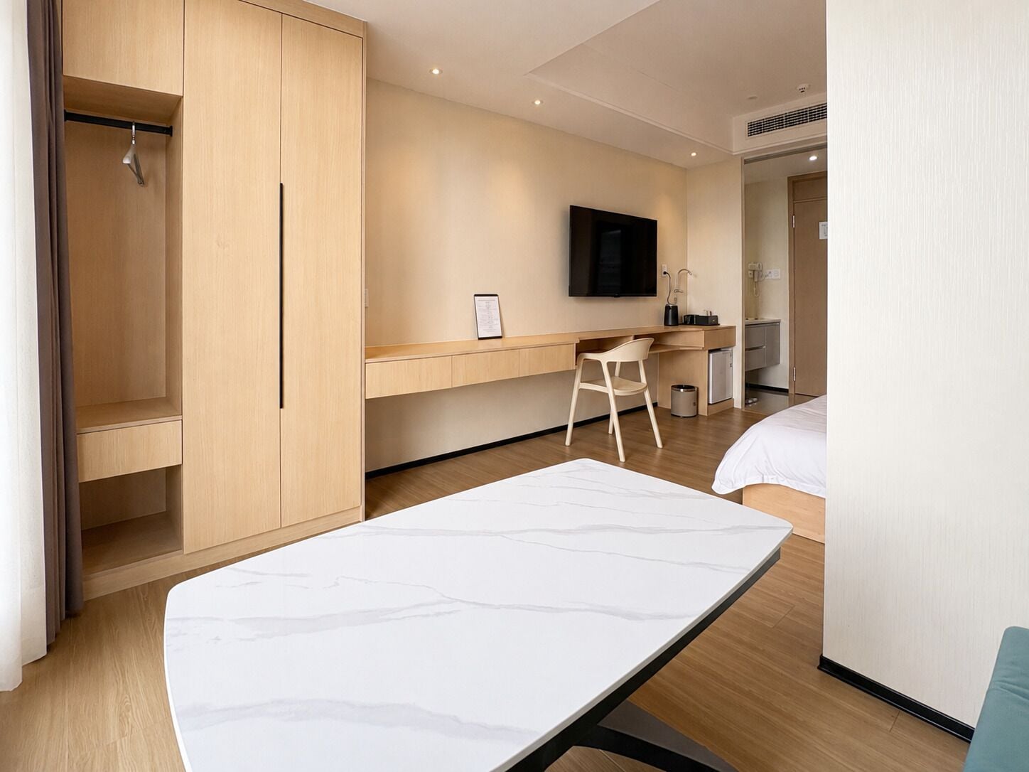 Una habitación de hotel moderna con cama, escritorio, silla, televisor y armario.