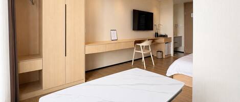 Una habitación de hotel moderna con cama, escritorio, silla, televisor y armario.