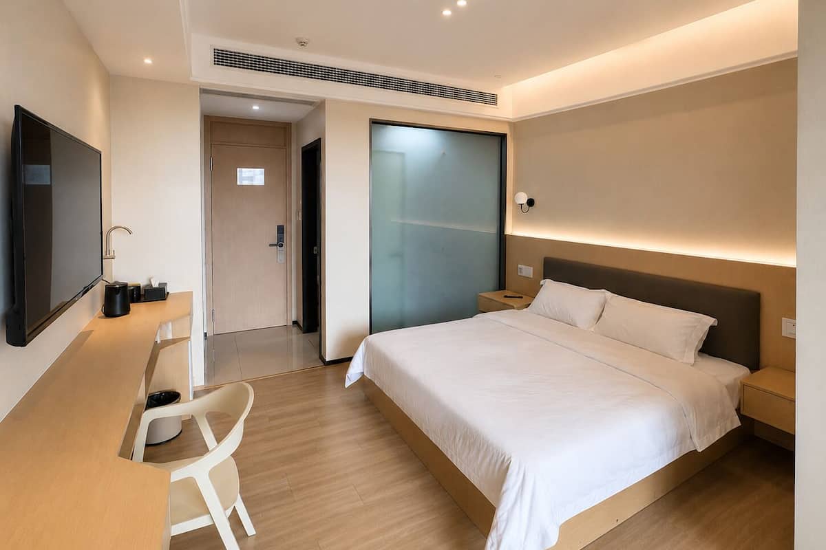 A modern hotel room with a bed, bedside tables, a desk with a chair, a flat-screen TV, and a sliding door.