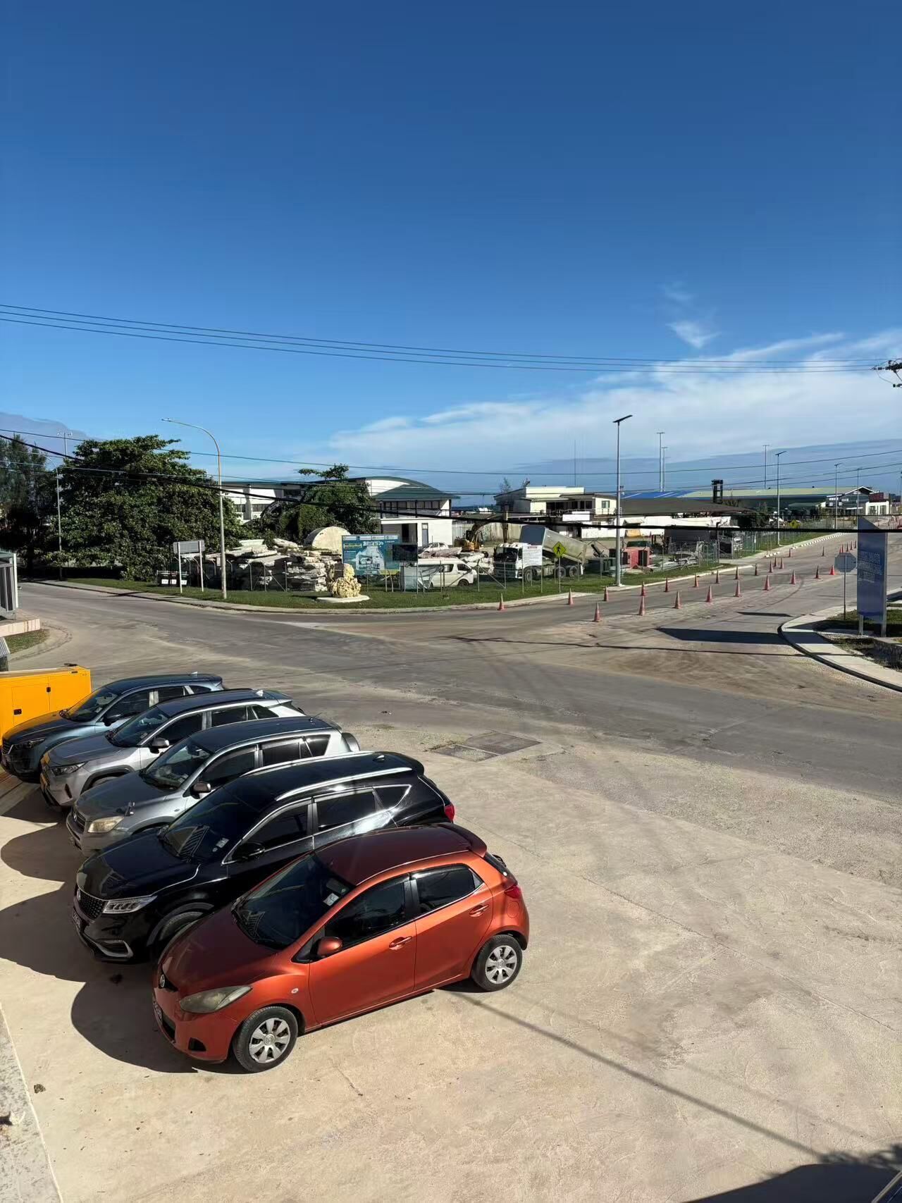 A parking lot with several cars, a clear sky, and buildings in the background.