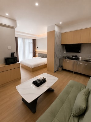 Una camera d'albergo moderna con un letto, una poltrona, un angolo cottura e una televisione.