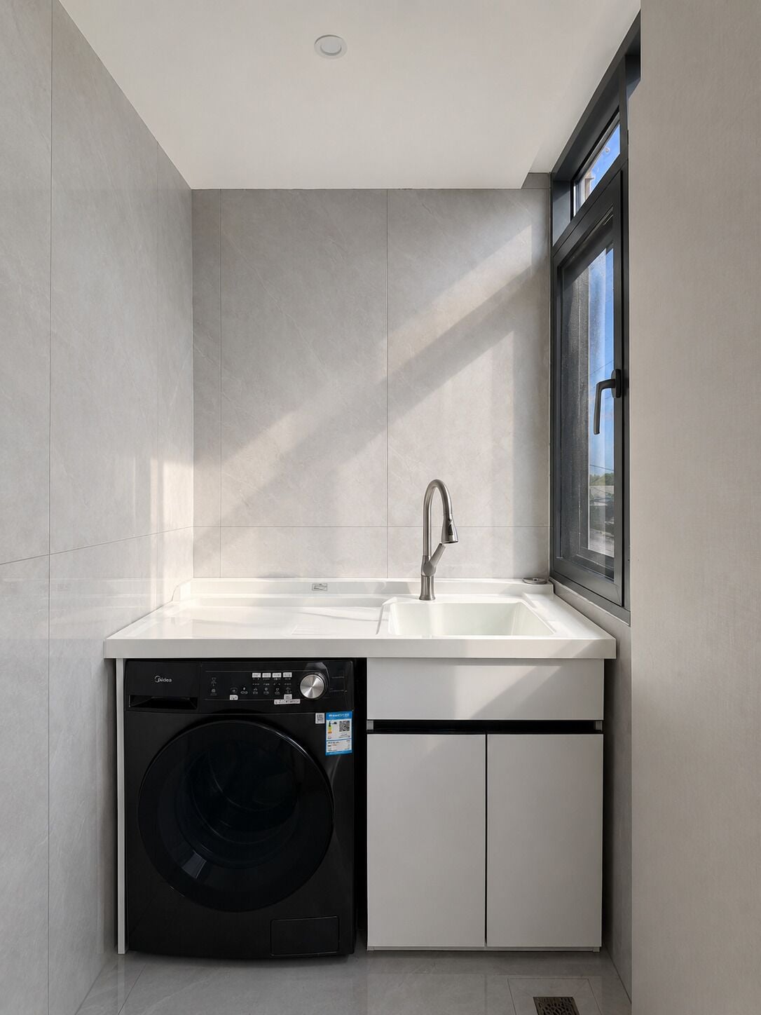 Cocina compacta con lavadora integrada, un lavabo y un ventanal.