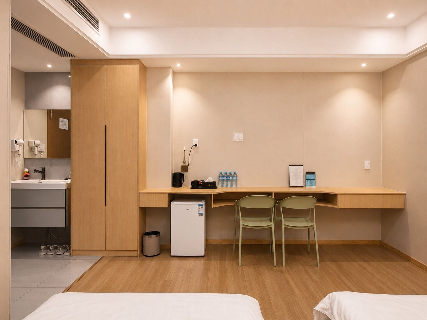 Habitació d'hotel amb escriptori de fusta, dues cadires, nevera petita, paperera, rentapel oberts i llit.