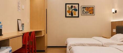 Habitación de hotel con un escritorio de madera, dos camas, una silla roja y dos obras de arte colgadas en la pared.