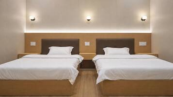 A hotel room with two single beds, wooden headboards, and wall-mounted light fixtures.