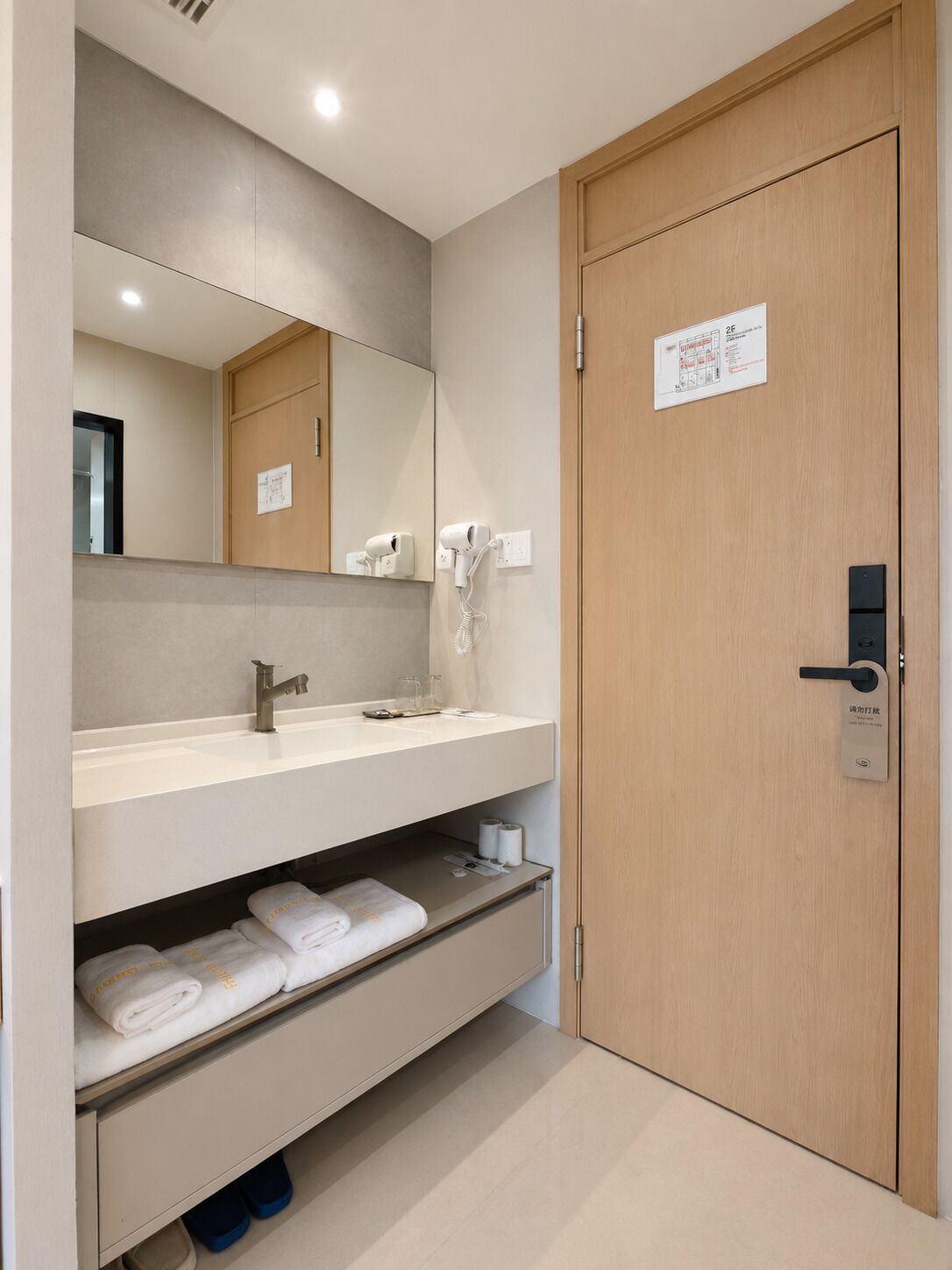 A hotel bathroom with a sink, mirror, hairdryer, towel rack, and a door with a lock.