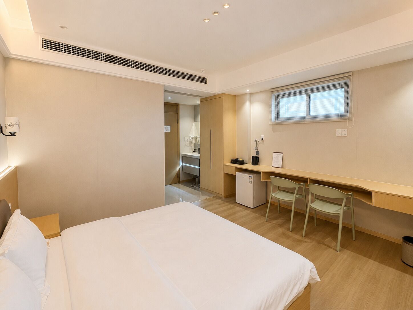 Une chambre à coucher comprenant un lit, un bureau, deux chaises, un petit réfrigérateur et une fenêtre avec des stores.