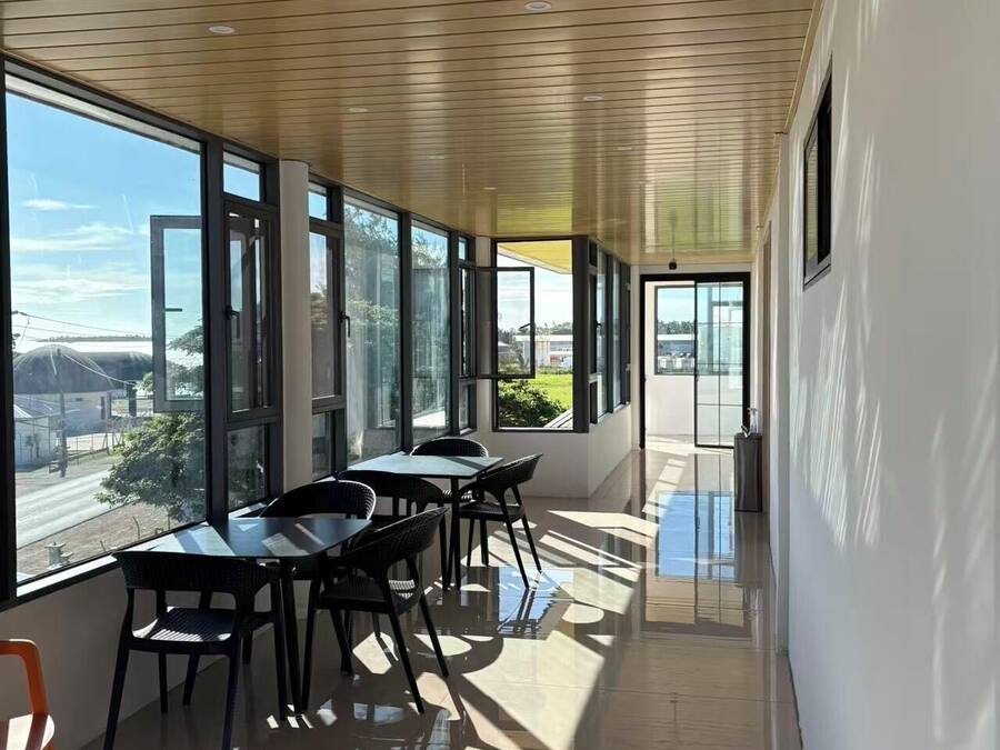 A modern interior with a long corridor, large windows, and a dining area with chairs and tables.