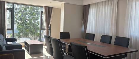 A conference room with a long table, black chairs, a sofa, and large windows with curtains.
