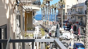 A balcony with a view of the street, palm trees, and a building with visible balconies and windows. - Sunny Ensuite by the Sea - A1, Saint Paul's Bay, Malta (Saint Paul's Bay)