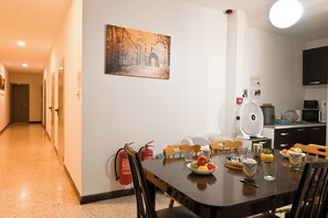A dining area with a table set for two, a fire extinguisher mounted on the wall, and a kitchen area with a microwave and a fan. - Sea Breeze Bay Guesthouse - A1, Saint Paul's Bay, Malta (Saint Paul's Bay)
