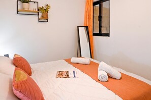 A neatly made bed with a white and orange bedspread, two rolled white towels, and a small booklet on the bed. - A Sunny Seaview In Central Sliema, Sliema, Malta (Sliema)
