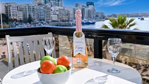 Un balcon avec une table, une bouteille de champagne et un saladier de fruits.