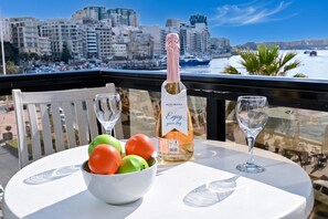A balcony with a table, a bottle of champagne, and a bowl of fruit. - A Sunny Seaview In Central Sliema, Sliema, Malta (Sliema)
