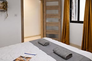 Habitació d'hotel amb un llit, una finestra amb cortines i una porta amb un panell de vidre mat.