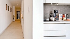 Un couloir mène à une cuisine au design moderne, équipée d’une hotte en acier inoxydable, d’une bouilloire et de divers appareils de cuisine.
