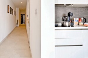A hallway leading to a kitchen with a modern design, featuring a stainless steel range hood, a kettle, and various kitchen appliances. - A Sunny Seaview In Central Sliema, Sliema, Malta (Sliema)