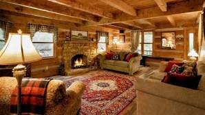 L’intérieur d’un chalet confortable, avec une cheminée en pierre, des poutres en bois et un grand tapis.
