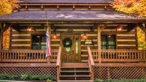 Une cabane en rondins avec une véranda, des marches et un drapeau.