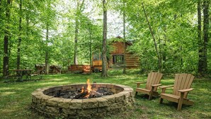 Un cadre extérieur rustique agrémenté d’un foyer en pierre, d’une terrasse en bois et de fauteuils Adirondack.