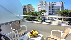 En balkon med hvide plastikstole, et lille bord og en kurv med frugt.