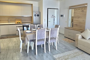 A modern kitchen with a built-in oven, a refrigerator, and a dining area with a table set for four. - Holiday Apartment in Golem 070, Durres, Albania (Durres)
