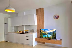 A modern kitchen with white cabinets, a wooden accent wall, and a flat-screen TV mounted on a wooden console.