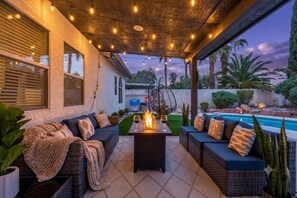 An outdoor patio with a fire feature, seating, and a pool view. - Las Vegas Oasis: Pool, Game Room, Arcade, EV Charging  (Las Vegas)
