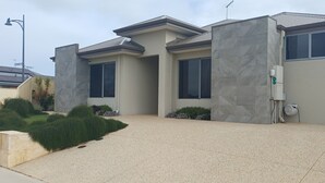A modern two-story house with a stone facade, large windows, and a landscaped front yard. - Cosy Haven - Large Comfy Dwelling, Close to Beach, Shops and Golf Course (Madora Bay)