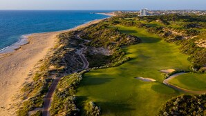 A coastal golf course with a view of the ocean, a road, and a building in the distance.