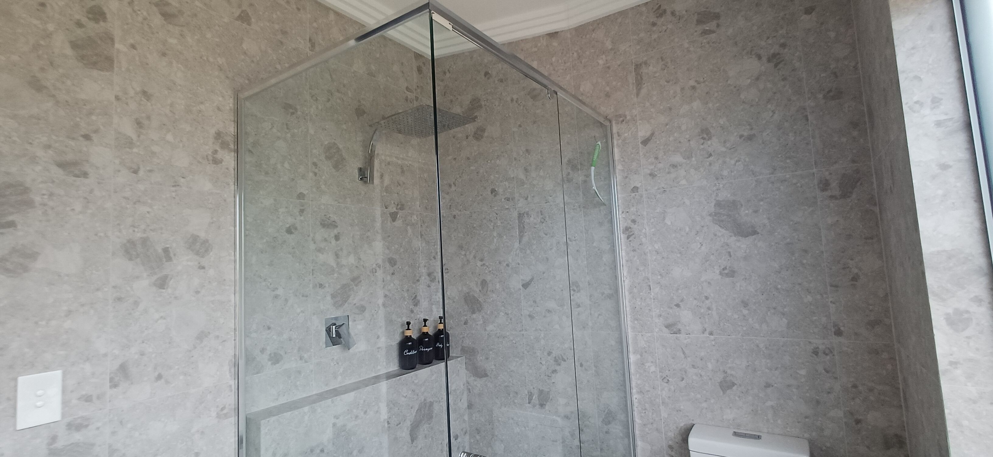 A modern bathroom with a glass-enclosed shower, marble walls, and a toilet.