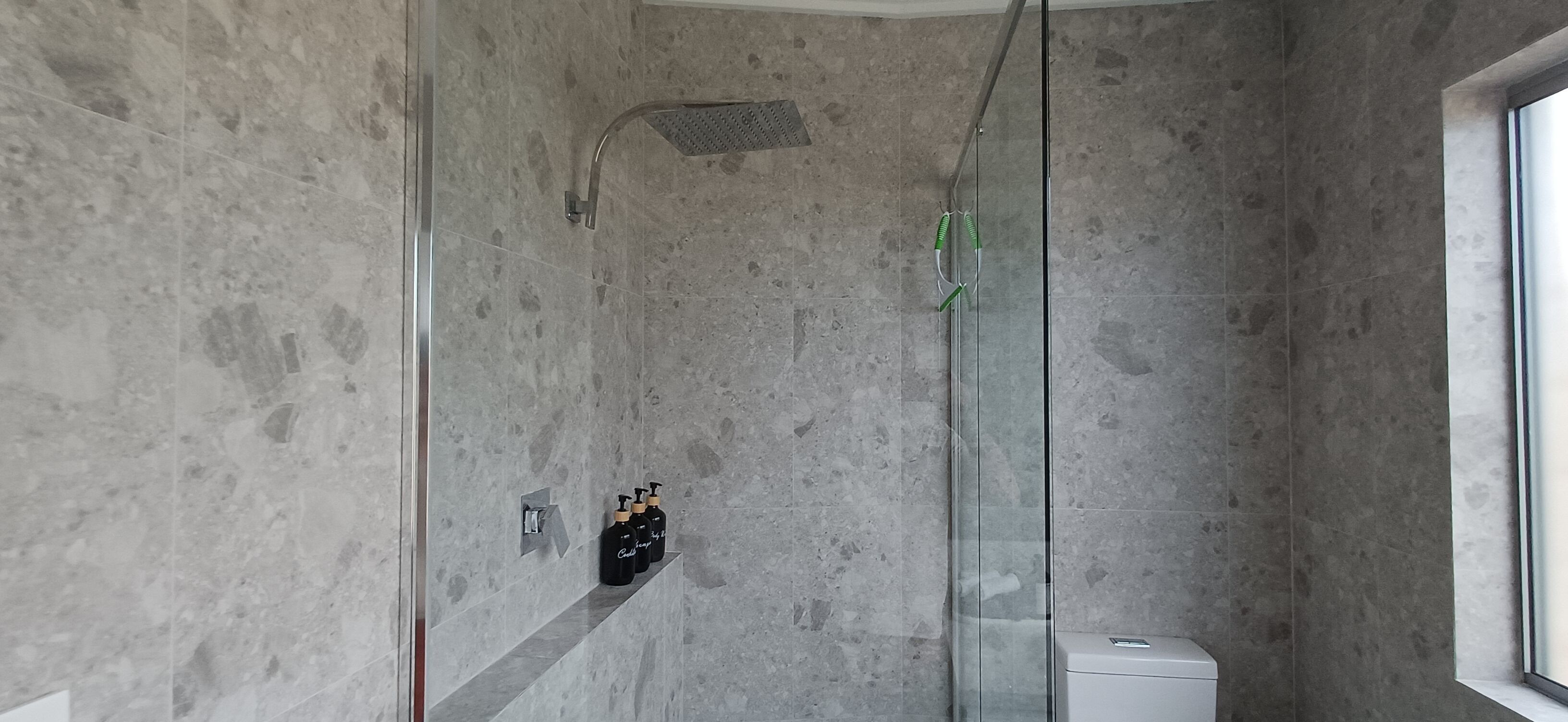 Et moderne badeværelse med brusekabine i glas, marmorvægge og toilet.