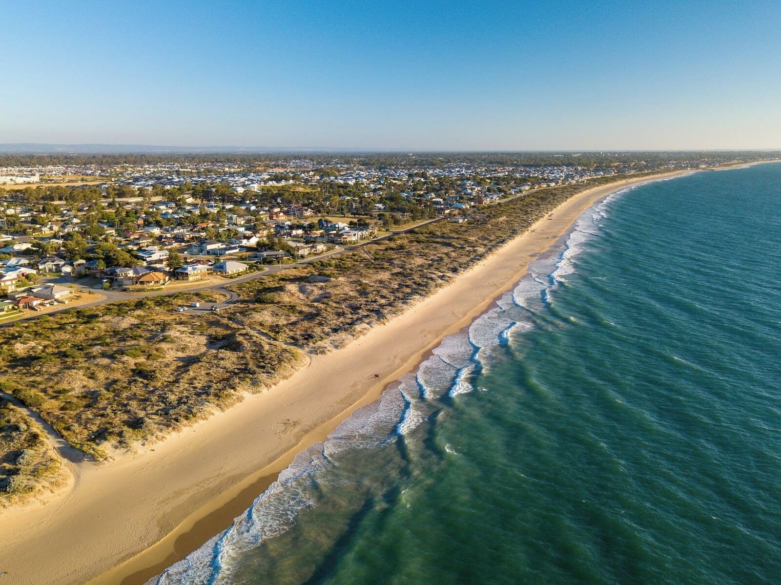Luchtbeeld van een kustplaatsje met een lang, zandstrand en een heldere blauwe zee.