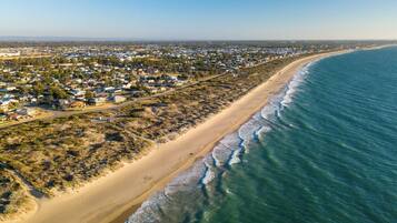 Luchtbeeld van een kustplaatsje met een lang, zandstrand en een heldere blauwe zee.
